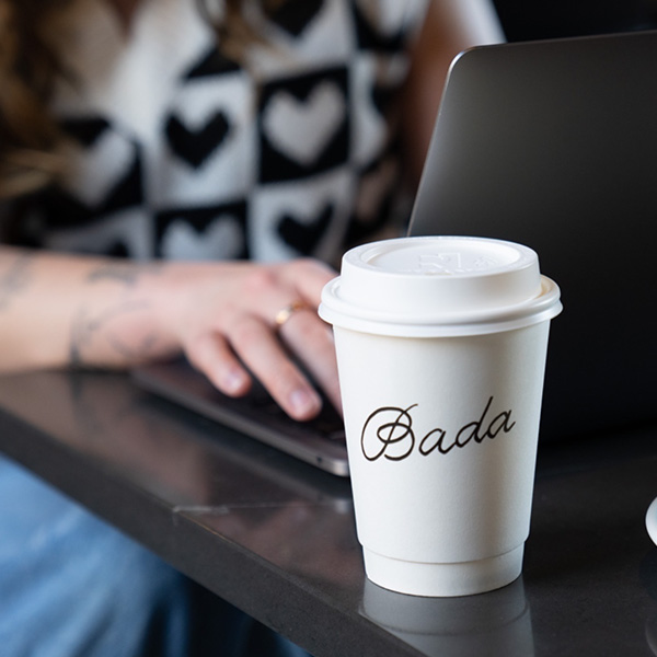 A person typing on a laptop with a coffee cup labeled Bada in the foreground.